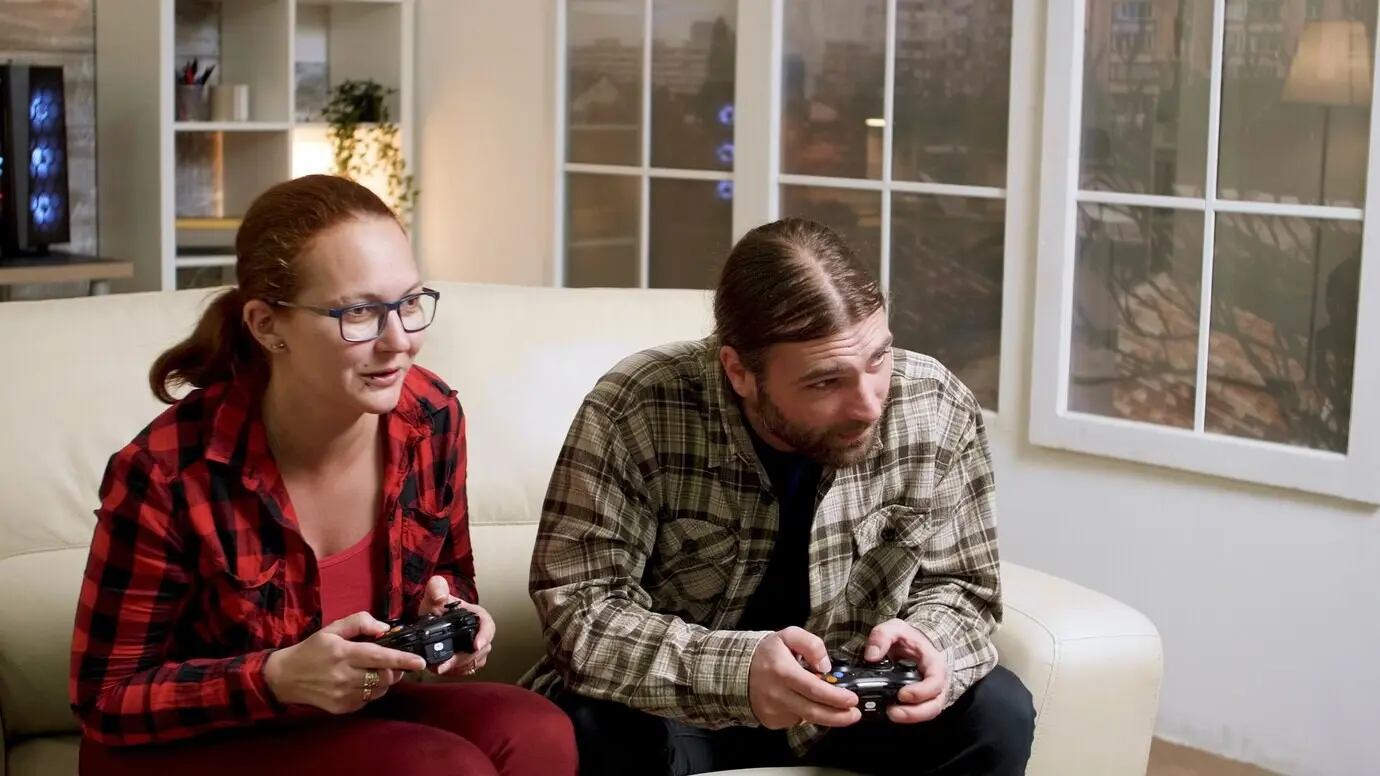 Ein Hipster-Paar sitzt auf dem Sofa und spielt Videospiele mit einem kabellosen Controller. Mann und Frau geben sich ein High-Five.